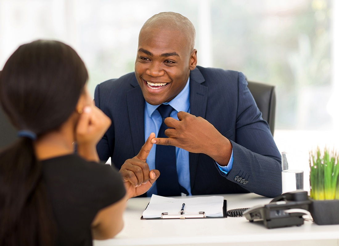 Business Insurance - Friendly Business Professional Sits at His Desk While Speaking With a Client